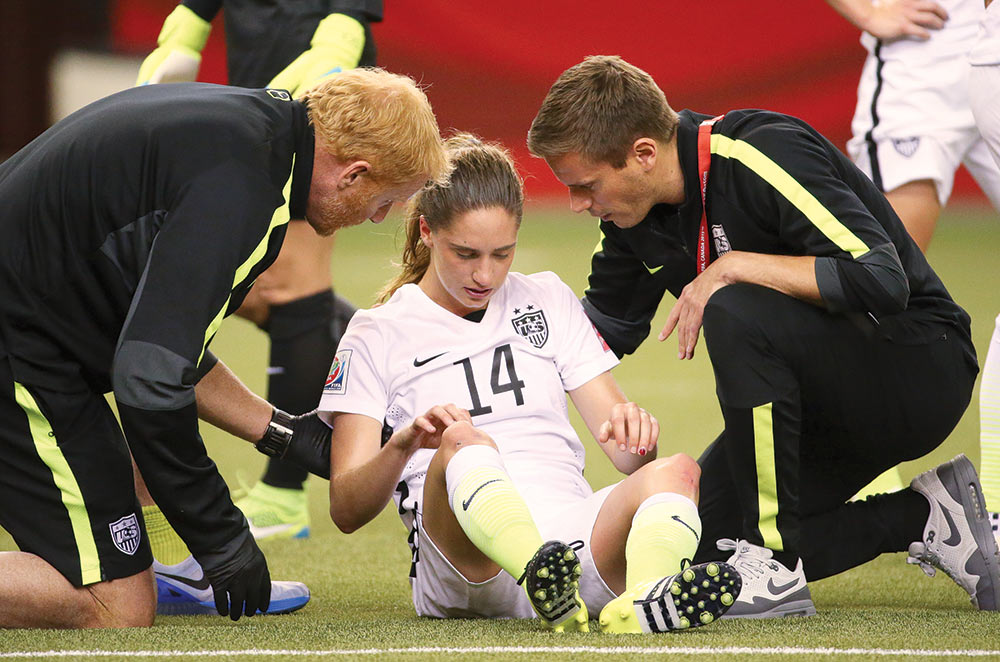 SCARY MOMENT: U.S. women’s national soccer team physician Bojan Zoric (right) and athletic trainer Rick Guter attend to midfielder Morgan Brian after her head collided with that of an opposing team player in a 2015 World Cup semifinal game. (Photo: Jean-Yves Ahern/USA Today Sports)